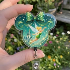 Puede incluir: Un portatarjetas verde y turquesa con Tinkerbell en forma de orejas de Mickey. El diseño incluye un lazo verde, un castillo y estrellas. El portatarjetas tiene un cordón retráctil.