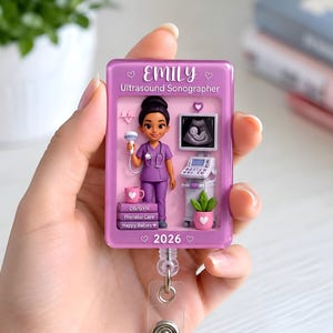 Op de afbeelding: Een rechthoekige roze badgehouder met een cartoon-echoscopist, een medische monitor met een foetus, en de tekst EMILY, Ultrasound Sonographer, OB/GYN, Prenatal Care, Happy Babies en 2026 met hartjes als decoratie.