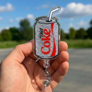 May include: A Diet Coke can-shaped badge reel with a glittery silver background and the Diet Coke logo in red. The badge reel has a clear plastic retractable cord and a clear plastic clip.