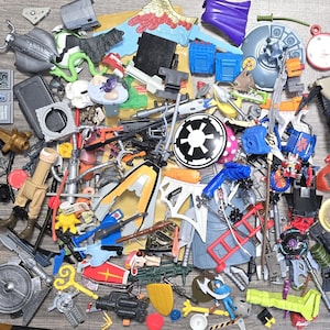 May include: A collection of colorful toy action figures and accessories, including weapons, vehicles, and character parts. The assortment features various colors, shapes, and sizes, suggesting a variety of play sets and themes.