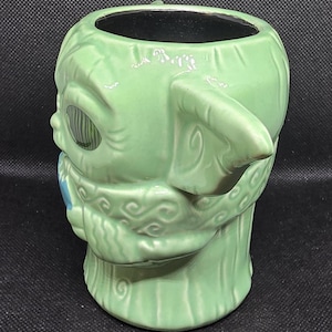 May include: A green ceramic mug shaped like a character from a popular science fiction franchise. The mug has large ears, a detailed face, and a textured surface. The interior of the mug is black.