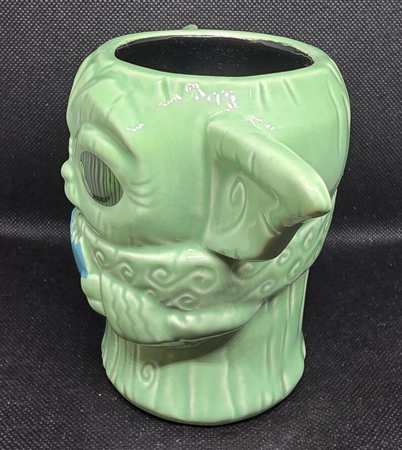 May include: A green ceramic mug shaped like a character from a popular science fiction franchise. The mug has large ears, a detailed face, and a textured surface. The interior of the mug is black.