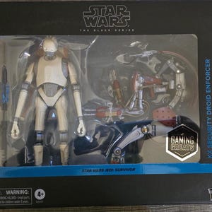 May include: A Star Wars Black Series action figure set featuring a KX Security Droid Enforcer and a Droideka. The figures are in a clear plastic display case with a black background. The packaging includes the text "Star Wars Jedi: Survivor."