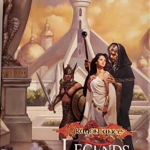 以下が含まれることがあります： ファンタジーシーンが描かれた本の表紙。白いドレスの女性、剣を持った戦士、ローブ姿の人物。タイトル「Dragonlance Legends Trilogy」は、ドラゴンのエンブレムとともに表示されています。