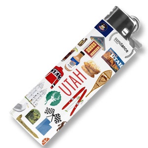May include: A white lighter with a silver top and a colorful design featuring various icons representing Utah. The design includes a red and white ski jacket, a green deer, a red and white ski, a blue and white snowshoe, a red and white house, a blue and white state flag, a red and white 'UTAH' text, and a red and white 'sundance' text.