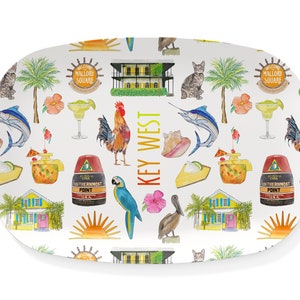 May include: A white oval serving platter with a colorful pattern of Key West icons. The pattern includes a rooster, a parrot, a pelican, a conch shell, a sunset, a margarita, a Key West house, a palm tree, a marlin, and the words "Key West".