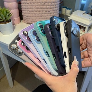 May include: A collection of colorful phone cases in various shades, including pink, purple, blue, green, and black. The cases have cutouts for the camera and buttons, and are made of a smooth, glossy material. The cases are designed to fit a smartphone.