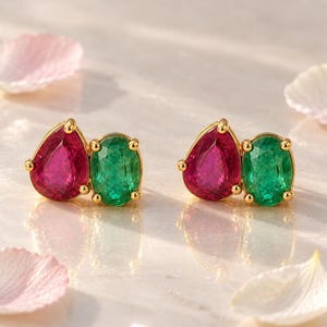 Può includere: Un paio di orecchini a lobo con montatura dorata, caratterizzati da una gemma rosa intenso a forma di pera e una gemma ovale verde brillante affiancate. Le pietre sono fissate da piccole griffe dorate che ne definiscono il design.