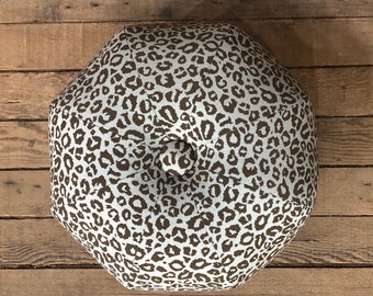 May include: A round, light gray and brown patterned ottoman with a brown button in the center.
