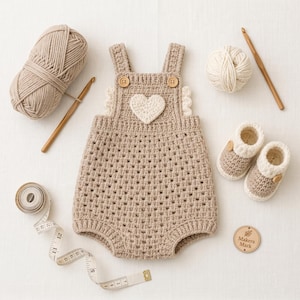 May include: A beige crochet romper with a white heart appliqu&eacute;, two wooden buttons, and ruffled sides. Accompanied by a ball of beige yarn, a ball of white yarn, two wooden crochet hooks, a measuring tape, and a wooden tag labelled Makers Mark.