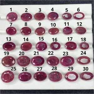 Puede incluir: Una colección de treinta piedras preciosas facetadas de forma ovalada, de color rojo rosado, dispuestas en una cuadrícula sobre una bandeja blanca. Cada piedra está numerada del 1 al 30, mostrando tonos de rojo y estructuras cristalinas.