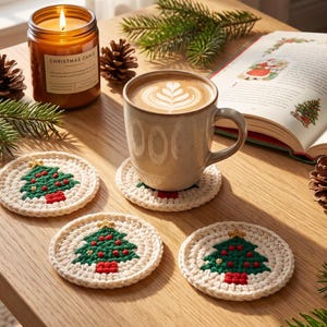 Puede incluir: Un juego de cuatro posavasos redondos de ganchillo en color crema, cada uno con un diseño de árbol de Navidad verde con adornos rojos y una estrella amarilla en la punta. Un posavasos sostiene una taza de cerámica con café.