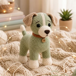 Può includere: Un cane all'uncinetto fatto a mano nei toni del verde, crema e marrone. Il cane ha un collare marrone con un'etichetta a forma di cuore. Il cane è in piedi su una coperta di maglia color crema. Lo sfondo include una piccola pianta in vaso e luci a corda.