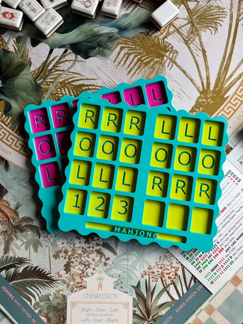 May include: Two teal plastic Mahjong organizers with scalloped edges. The top tray features a lime green interior with grid compartments labeled with the letters R, O, L, and the numbers 1, 2, 3. The word MAHJONG is embossed at the bottom center.