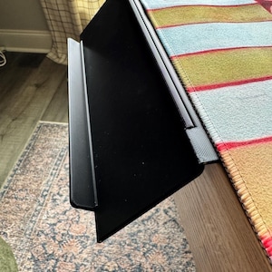 Puede incluir: Una bandeja de extensi&oacute;n de escritorio de pl&aacute;stico negro con una superficie plana y un borde frontal elevado, dise&ntilde;ada para fijarse al borde de una mesa. La bandeja presenta un acabado texturizado y un soporte de montaje resistente.
