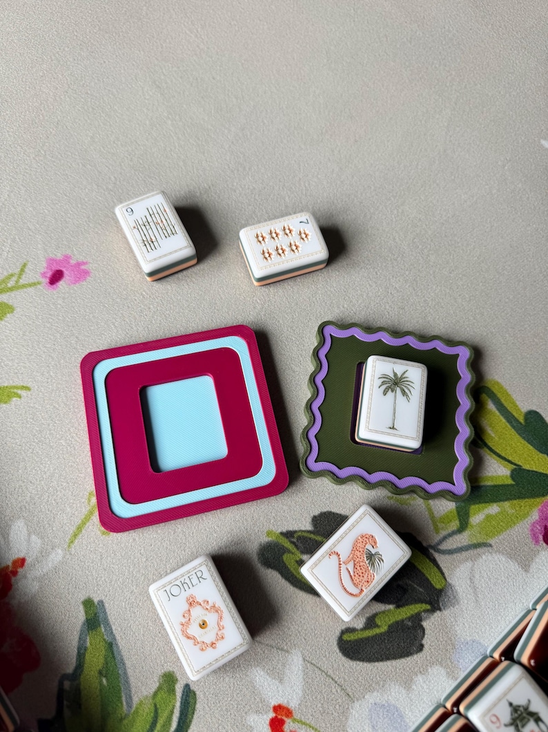 May include: A collection of decorative Mahjong tiles and coasters. The tiles feature various designs, including a palm tree, a leopard, and the word "Joker." The coasters are in shades of pink, blue, and green.