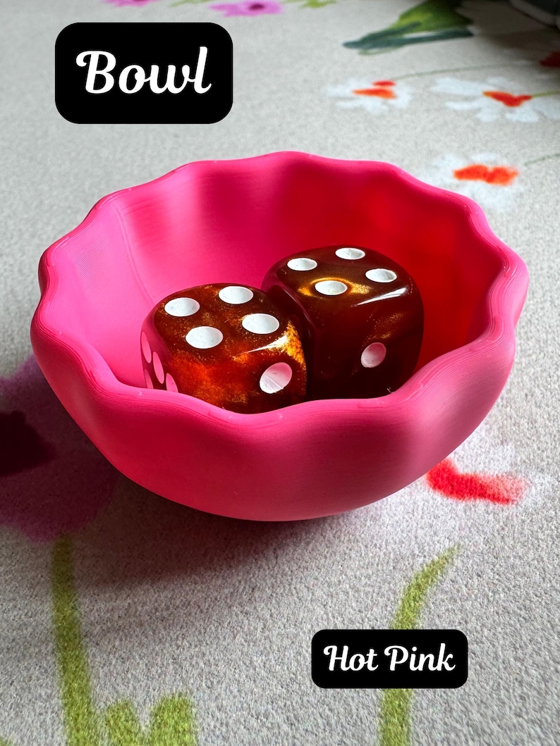 May include: A hot pink bowl with a scalloped edge containing two amber-colored dice with white pips. The image includes the text Bowl and Hot Pink. The bowl has a smooth, matte finish and a rounded shape, while the dice feature a translucent, marbled appearance.