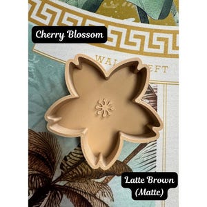 May include: A matte latte brown cookie cutter shaped like a five-petaled cherry blossom flower. The cutter features a central stamens detail and has a 3D printed texture. The text Cherry Blossom and Latte Brown (Matte) is visible in the image.