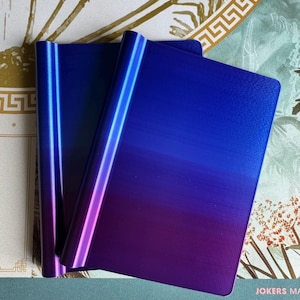 May include: Two rectangular metal plates featuring a smooth gradient finish that transitions from a deep royal blue at the top to a vibrant purple at the bottom. The plates have a curved, rounded edge on one side and a flat, straight edge on the other.