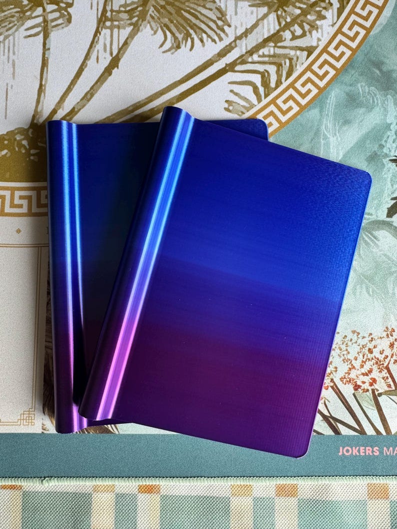 May include: Two rectangular metal plates featuring a smooth gradient finish that transitions from a deep royal blue at the top to a vibrant purple at the bottom. The plates have a curved, rounded edge on one side and a flat, straight edge on the other.