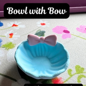 May include: An ice blue matte bowl featuring a sakura pink matte bow attached to the rim. The bowl has a textured, ridged surface. Text on the image reads: Bowl with Bow, and Ice Blue (Matte)/Sakura Pink (Matte). The bowl is circular in shape.