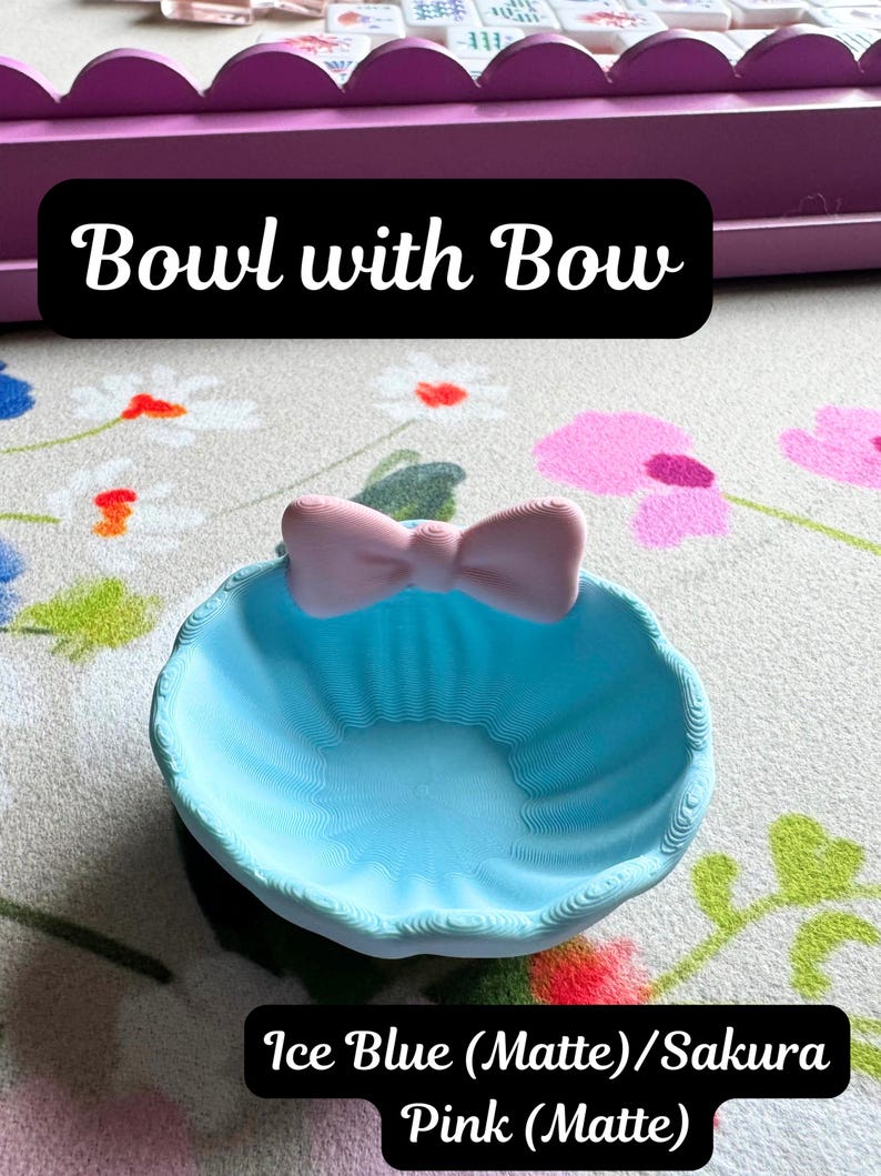 May include: An ice blue matte bowl featuring a sakura pink matte bow attached to the rim. The bowl has a textured, ridged surface. Text on the image reads: Bowl with Bow, and Ice Blue (Matte)/Sakura Pink (Matte). The bowl is circular in shape.