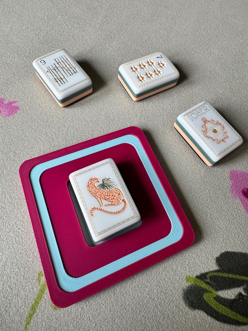 May include: A set of playing cards with a cheetah illustration, a card with the word "JOKER", and other cards with numbers and symbols. The cards are white with a peach and teal border, and are on a magenta and teal tray.