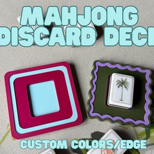 May include: A close-up of two Mahjong discard deck holders. One is a square with a magenta frame and a light blue interior. The other is a green frame with a purple scalloped edge, holding a white tile with a palm tree. Text reads "MAHJONG DISCARD DECK" and "CUSTOM COLORS/EDGE".