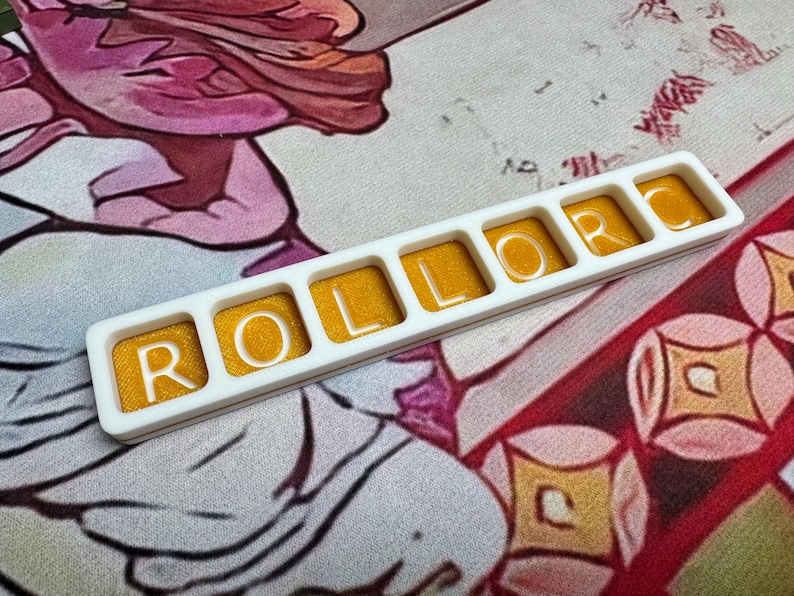 May include: A rectangular white plastic frame containing six individual square compartments, each filled with a shimmering golden-yellow resin. The white letters R, O, L, L, O, R are embedded within the resin, spelling out the word ROLLOR.