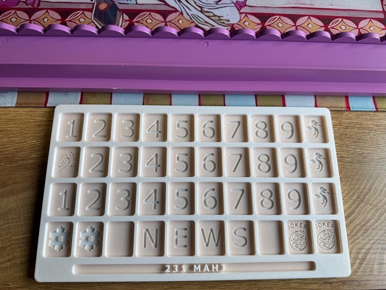 May include: A beige number and letter tray with embossed numbers, letters, and symbols. The tray includes the word "NEWS", the numbers "231", and the word "MAH". The tray also features snowflake, bird, and joker symbols.
