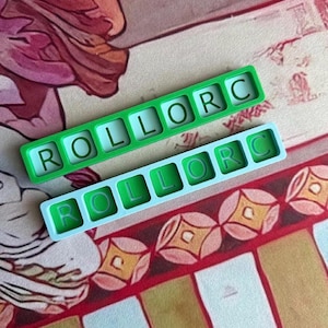 May include: Two rectangular silicone molds, one in bright green and one in light blue, each featuring six square cavities arranged in a single row. Each cavity contains a raised letter, spelling out the word ROLLORC in a clear, sans-serif font.