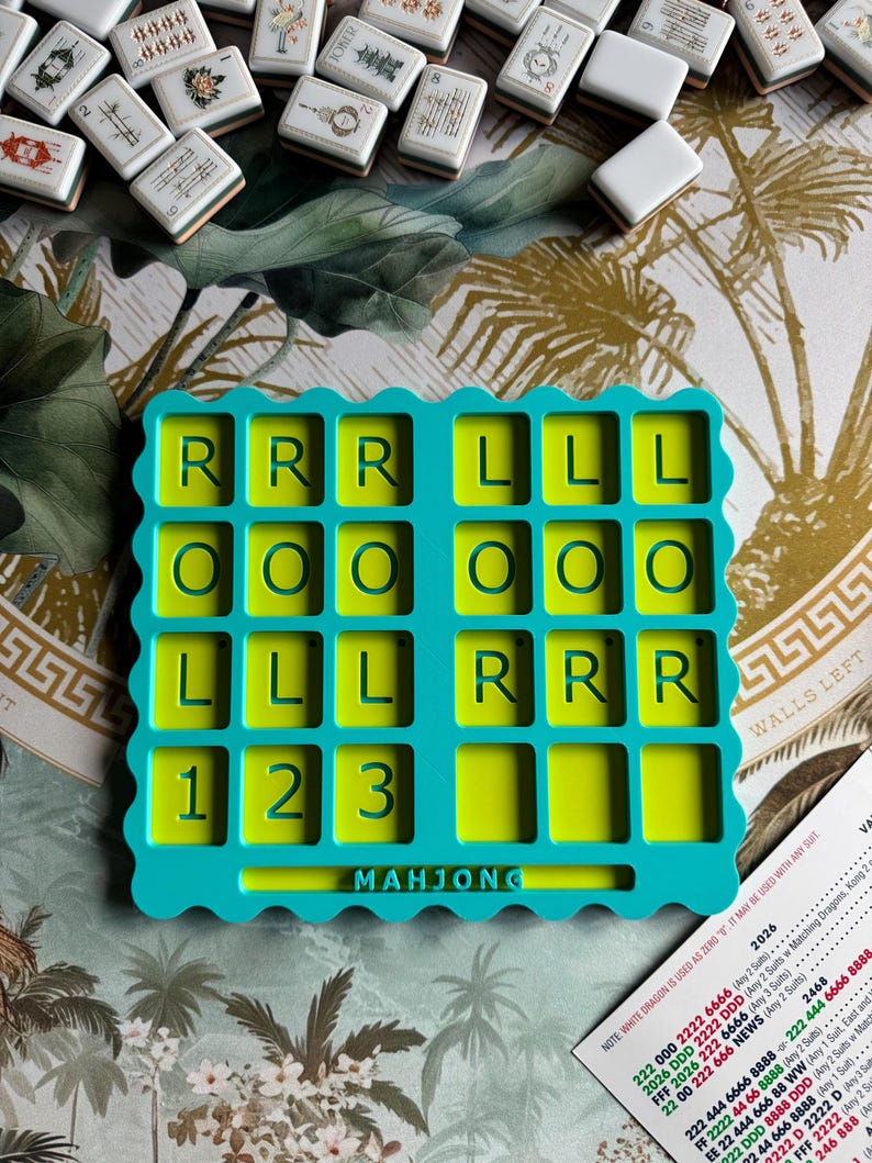 May include: A teal and lime green Mahjong scorekeeping tray with a scalloped edge. The tray features a grid of rectangular slots labeled with the letters R, L, O, and the numbers 1, 2, 3 in dark green. The word MAHJONG is embossed at the bottom center.