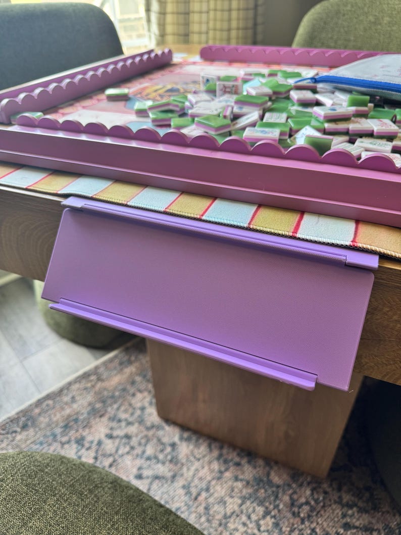 Puede incluir: Un soporte para fichas de pl&aacute;stico de color morado claro con forma rectangular y un borde frontal plano, dise&ntilde;ado para colgarse del borde de una mesa. El soporte presenta una superficie lisa y un dise&ntilde;o sencillo y funcional.