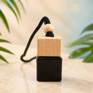 May include: A square black glass bottle with a light-coloured wooden cap and a small wooden bead on a black cord. The bottle is designed for hanging, featuring a smooth, dark finish contrasted by the natural grain of the wooden components.