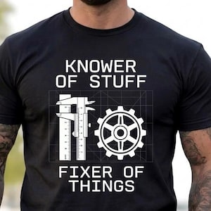 May include: A black short-sleeved t-shirt featuring white text that reads "KNOWER OF STUFF" above a graphic of a caliper and a gear, with the text "FIXER OF THINGS" below. The design includes a thin white grid pattern behind the mechanical icons.