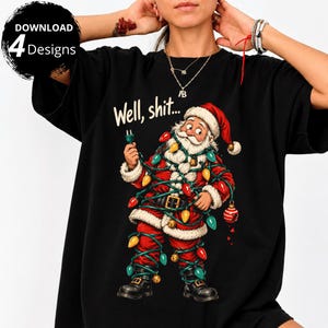 May include: A black t-shirt featuring a graphic of Santa Claus tangled in colorful Christmas lights, holding an electrical plug. Above the illustration, the text reads "Well, shit..." in a cream-colored font. The design includes red, yellow, green, and blue light bulbs.
