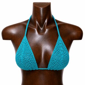 Può includere: Un top bikini all'uncinetto turchese esposto su un manichino di legno. Le coppe triangolari sono collegate da un filo sottile e anche le spalline all'americana sono all'uncinetto. La trama aperta dell'uncinetto crea un aspetto strutturato.