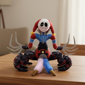 May include: A plush toy resembling a jester with a smiling face, red and blue attire, and claw-like hands. The toy features a red and white jester's hat and is positioned on a wooden surface.