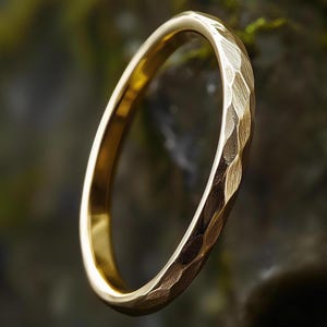 May include: A gold ring with a hammered texture. The ring has a bright, polished finish and a simple design. The ring is a classic piece of jewellery. The ring's diameter is approximately 2 cm.