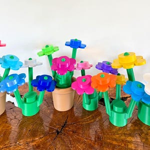 以下が含まれることがあります： 赤、青、黄色、ピンクなど、さまざまな色合いのカラフルなプラスチック製のフラワーアレンジメントのコレクション。 各花は緑色の茎の上にあり、小さな茶色のポットに入れられています。 花は木製の表面に配置されています。