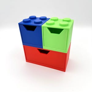 May include: A stack of three colorful storage drawers designed to resemble large toy building blocks. The top two drawers are blue and green, and the bottom drawer is red. Each drawer has a handle-shaped cutout.