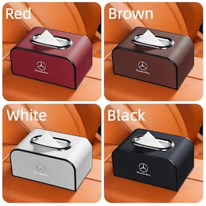 May include: A set of four car tissue box holders in red, brown, white, and black. Each box has a silver trim around the tissue opening and a Mercedes-Benz logo. The boxes are rectangular and appear to be made of leather.