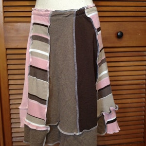May include: A patchwork skirt in shades of pink, brown, and tan. The skirt is made of various fabric panels, with a ruffled hemline. The skirt is displayed on a mannequin.