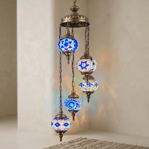 May include: A hanging chandelier with five mosaic glass globes in shades of blue and white. The globes are suspended from a bronze-colored metal fixture by chains. The mosaic design features star and diamond patterns, creating a warm, inviting glow.