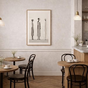 May include: A cafe interior with round wooden tables, black chairs, and a built-in bench. A framed artwork of three figures hangs on the wall. Decorative pendant lights hang above the tables. The cafe has a neutral color palette.