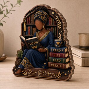 May include: A layered wooden decorative plaque featuring a person wearing a blue patterned robe and headwrap, reading a book titled NAOMI with a crown icon. Beside them are stacked books labeled READ, RISE, LEAD, CREATE, a mug, and the text Black Girl Magic.