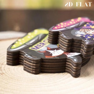 May include: A stack of layered wooden cutouts featuring cartoon illustrations of a witch and a cat with cauldrons. The top piece shows a character in a purple hat with yellow stars. The text 2D FLAT is visible in the upper right corner.