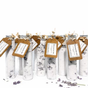 May include: Clear glass tubes filled with white bath salts and lavender buds, each with a brown tag tied with twine. The tags read "Relaxing bath salts". A few sprigs of lavender are scattered around the base of the tubes.