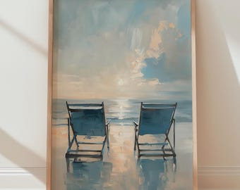May include: A framed art print depicts two blue beach chairs on a sandy shore, facing the ocean under a cloudy sky. The artwork is in a wooden frame and is displayed against a white wall and wooden floor.