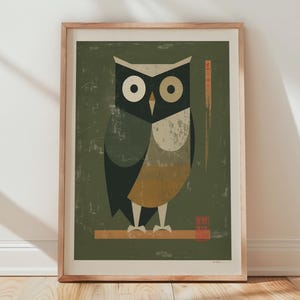 May include: Framed art print featuring a stylized owl illustration. The owl is depicted with geometric shapes in shades of black, white, and tan against a muted green background. The artwork is framed in a light wood frame and rests against a white wall.